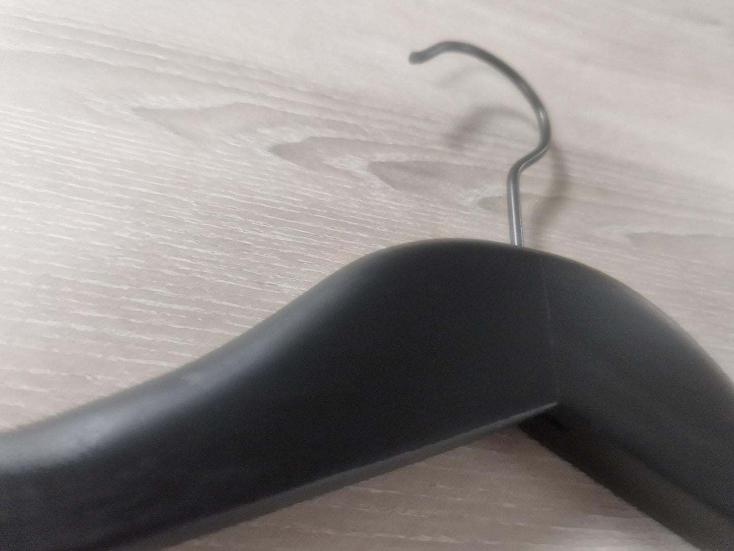 Close-up of a Hangers of London Wooden Black Jacket 39cm with a curved hook on a wooden surface. The hanger's smooth and curved design is clearly visible, and the wood grain of the surface adds texture to the background, making it perfect for an elegant jacket display.
