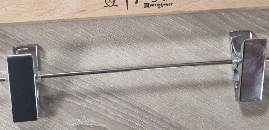 A close-up image of an untreated Wooden Natural Clip Branded Penguin 35cm with metal clips designed to hold pants or skirts. The hanger features the brand name "Hangers of London" printed on it, and the background is a textured gray surface.