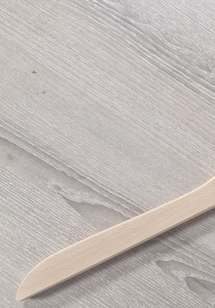 A light Wooden Natural Top Branded Penguin 43cm placed on a grey wood-grain surface. The angle of the Wooden Natural Top Branded Penguin 43cm shows the blade and a portion of the handle, emphasizing its smooth texture and simple design. There are slight natural wood imperfections visible on the surface, reminiscent of Hangers of London's charm.