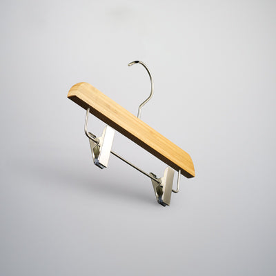 A Hangers of London Bamboo Wood Sustainable Clip Bottom Hanger 26cm is suspended against a light gray background. The bamboo wood hanger is designed for securing garments with the clips attached to the wooden bar at the bottom.