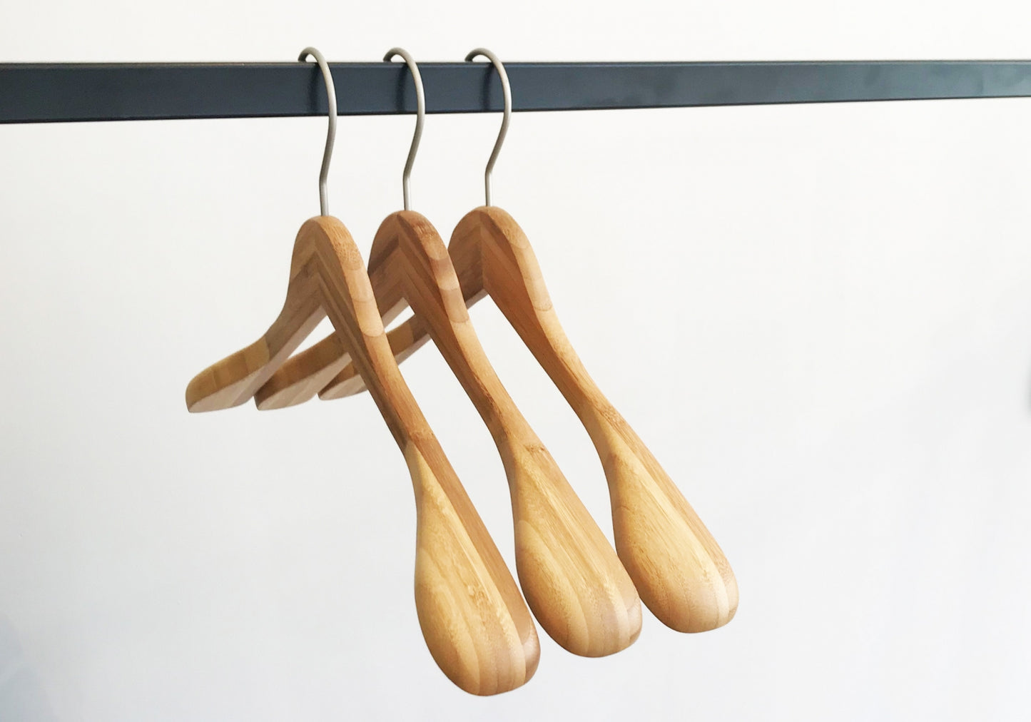 Three Hangers of London Bamboo Wood Sustainable Top Jacket Hanger 42cm are hanging on a black metal rod against a white background. The hangers are evenly spaced and have a smooth, polished finish.