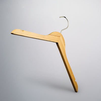 A Hangers of London Bamboo Wood Sustainable Top Hanger with Notch 42cm, featuring a silver metal hook, is suspended against a light grey background. The hanger has notches on both ends, ideal for securing straps of clothing. The design is simple and functional.