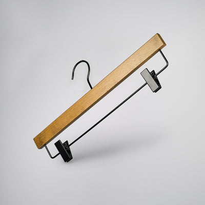 A Hangers of London Dark Wood Sustainable Bottom Trouser Skirt Hanger With Clips 37cm, featuring strong metal clips and a metal hook, is suspended against a light gray background. The hanger is angled with the hook pointing upwards and the clips positioned at the bottom.