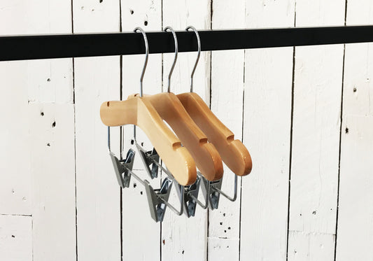 Three Hangers of London Natural Wood Coat Kids Hanger with Bar 28cm are hanging on a black rod against a white wooden plank wall. These high-quality hangers are evenly spaced and aligned in a row, ideal for organizing a child's wardrobe.