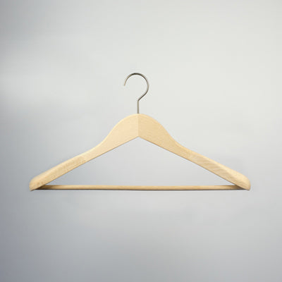 A high-quality, natural wood hanger with a metal hook is suspended against a neutral gray background. The Hangers of London Natural Wooden Jacket Hanger with Trouser Bar 44cm has a curved triangular shape with a sustainable suit bar at the bottom for hanging pants or skirts.