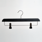 The Hangers of London Black Wooden 35cm Clip Hanger, shown in a pack of 100, features a sleek black and silver design with two adjustable clips for securely hanging pants or skirts, photographed against a plain white background.