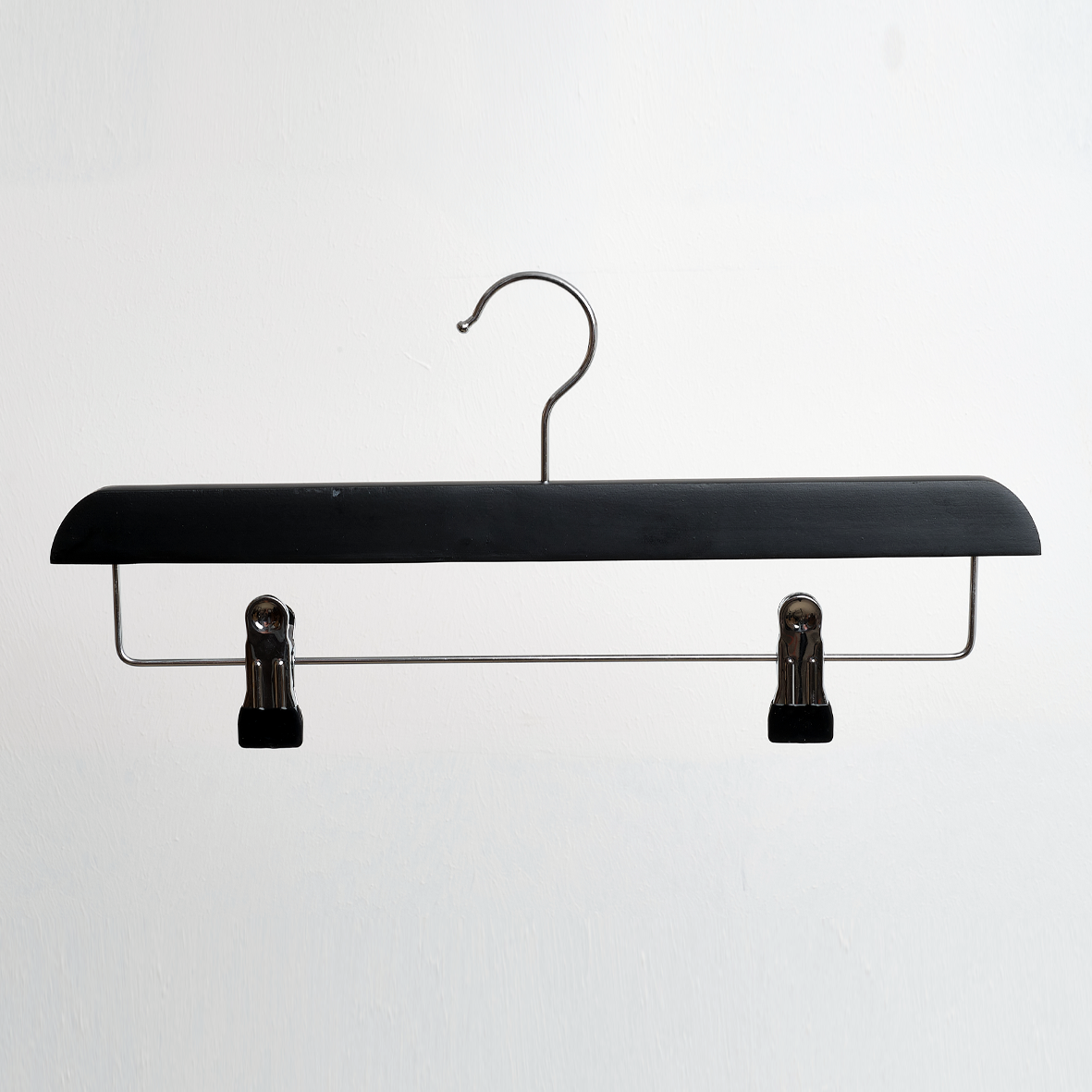 The Hangers of London Black Wooden 35cm Clip Hanger, shown in a pack of 100, features a sleek black and silver design with two adjustable clips for securely hanging pants or skirts, photographed against a plain white background.