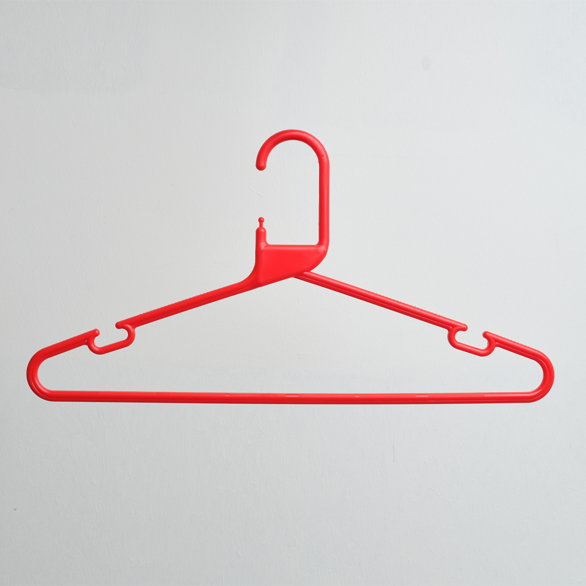 A Heavy Duty Economy Red Multi Purpose Rainbow Hanger by Hangers of London, made of plastic and featuring a hook, is displayed hanging against a plain white wall.