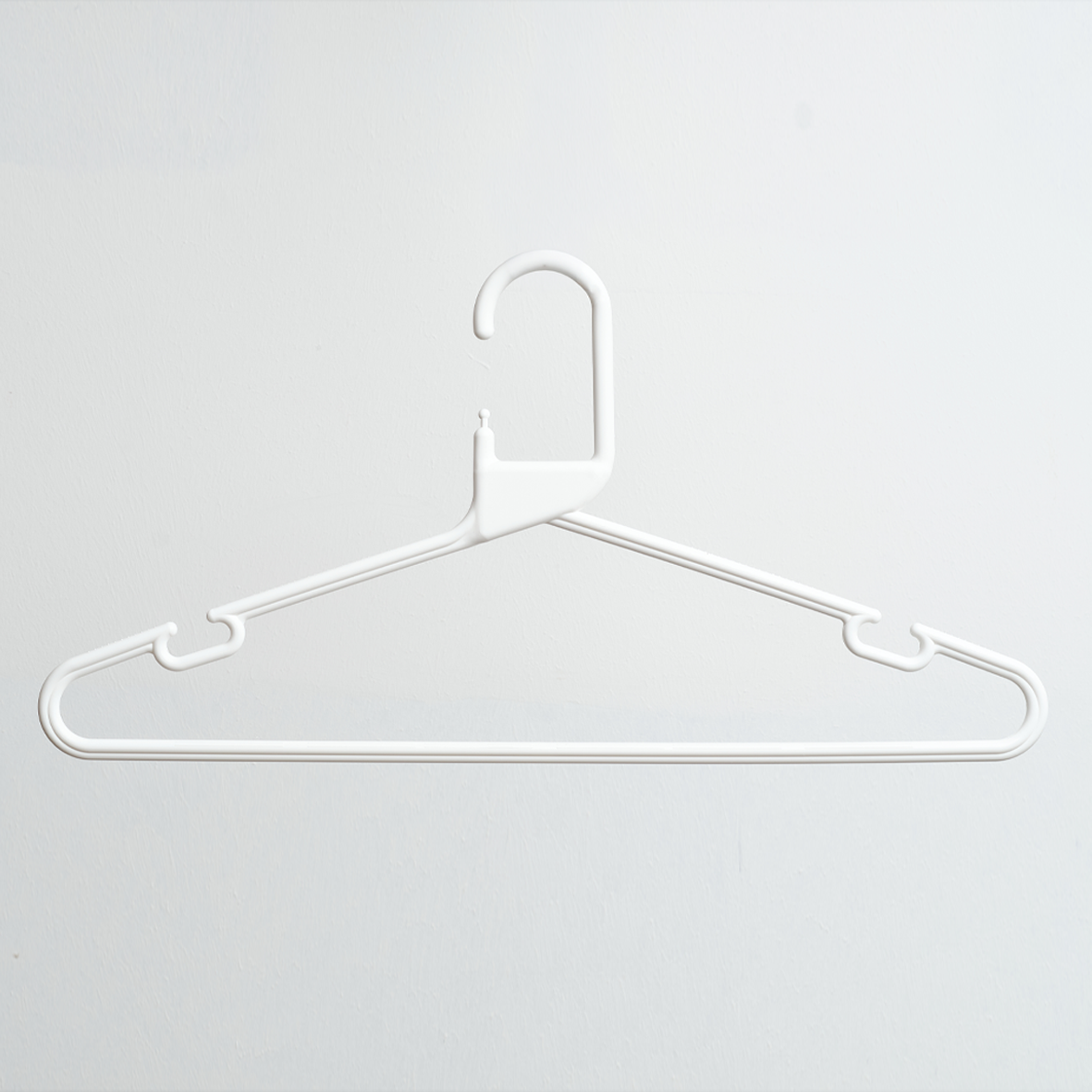 A Heavy Duty Economy White Multi Purpose Rainbow Hanger from Hangers of London is hanging on a plain, light-colored wall.