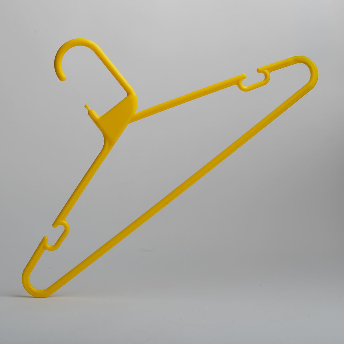 A Heavy Duty Economy Yellow Multi Purpose Rainbow Hanger by Hangers of London stands upright against a plain gray background. This plastic hanger features hooks on both sides and a curved top hook for easy hanging.