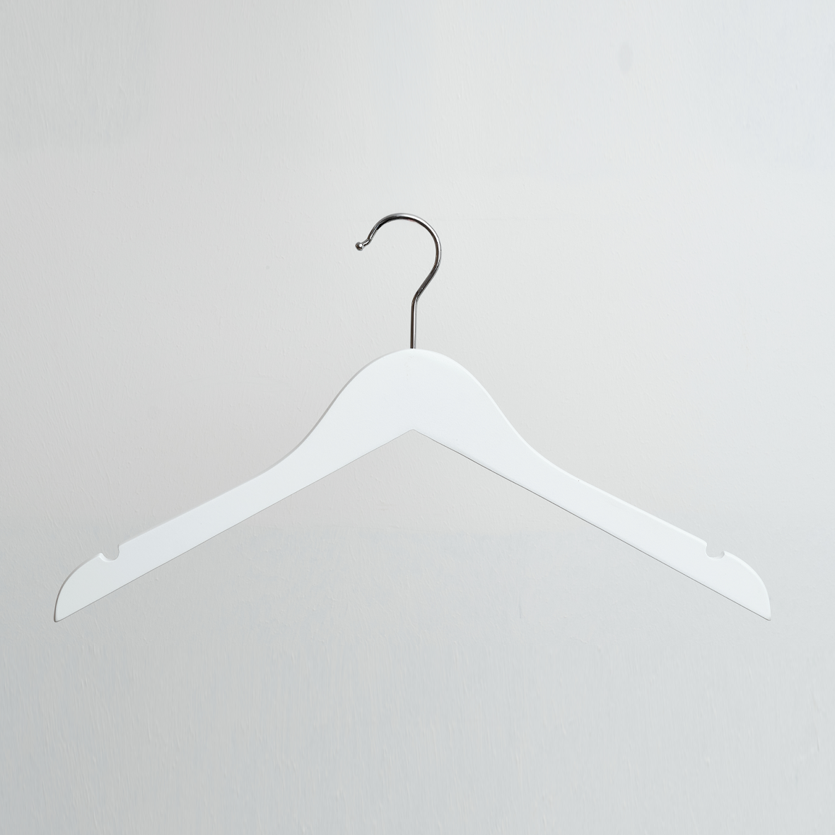 A Hangers of London White Wooden 40cm Top Hanger With Notches is displayed against a plain, light gray wall, its silver hook visible.