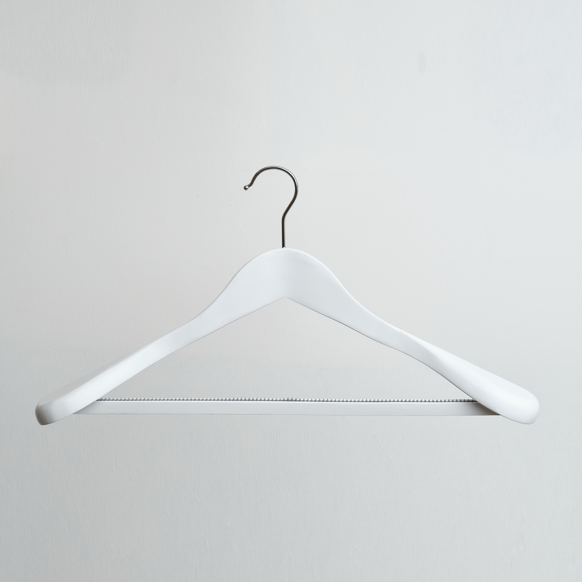 A White Wooden 45cm Jacket Hanger With Non Slip Trouser Bar by Hangers of London, featuring a metal hook, is displayed against a plain, light-colored wall.