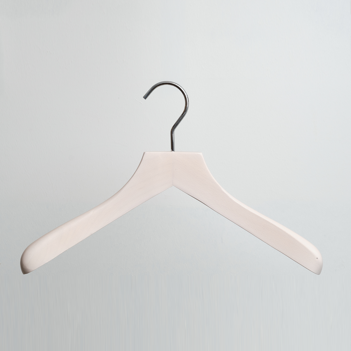 A Luxury Whitewashed FSC Certified Beech Wooden 41cm Jacket Hanger by Hangers of London, featuring a silver hook, is hanging against a light gray background.