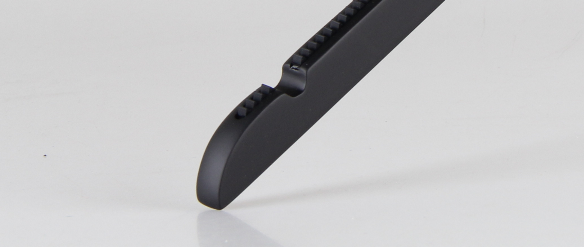 Close-up of the blade tip of a Hangers of London Wooden Rubber Soft Touch Black Kids Top (30cm) with ridges on the safety edge, resting against a white background. The rubberized finish enhances grip and control during use.