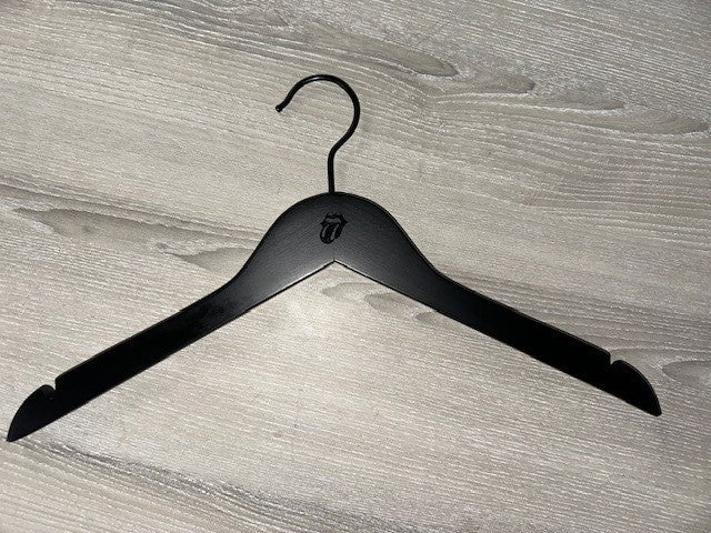 A Black Wooden top hanger branded Rolling Stones 38cm by Hangers of London, featuring their iconic tongue and lips design, sits on a gray wooden surface. Perfect for dresses or strapped shirts, this hanger comes in a pack of 50.