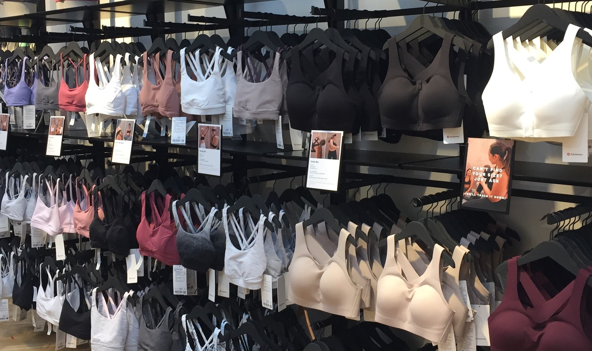 A store display showcasing a variety of Hangers of London Wooden Rubber Soft Touch Black Kids Top (30cm) in different colors and styles. The Wooden Rubber Soft Touch Black Kids Top (30cm) are hung neatly on wooden hangers across multiple rows. Some tags with product information are visible hanging from the Hangers of London products and attached to the display.