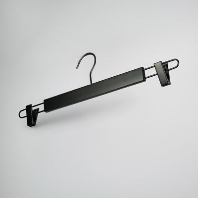 A Hangers of London Black Wooden Clip Bottom Hanger 37cm with two sturdy, adjustable clips, designed for hanging pants or skirts. The Hangers of London hanger features a hook at the top that offers 360-degree rotation for easy positioning on any rod or bar. It rests against a plain, light grey background.