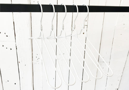 Four Hangers of London White Aluminium Top Hanger 40cm are neatly lined up on a black rod against a rustic white wooden wall. The rod is suspended horizontally, and the simple, minimalist design of these sturdy metal hangers stands out against the textured backdrop—perfect for a modern closet.